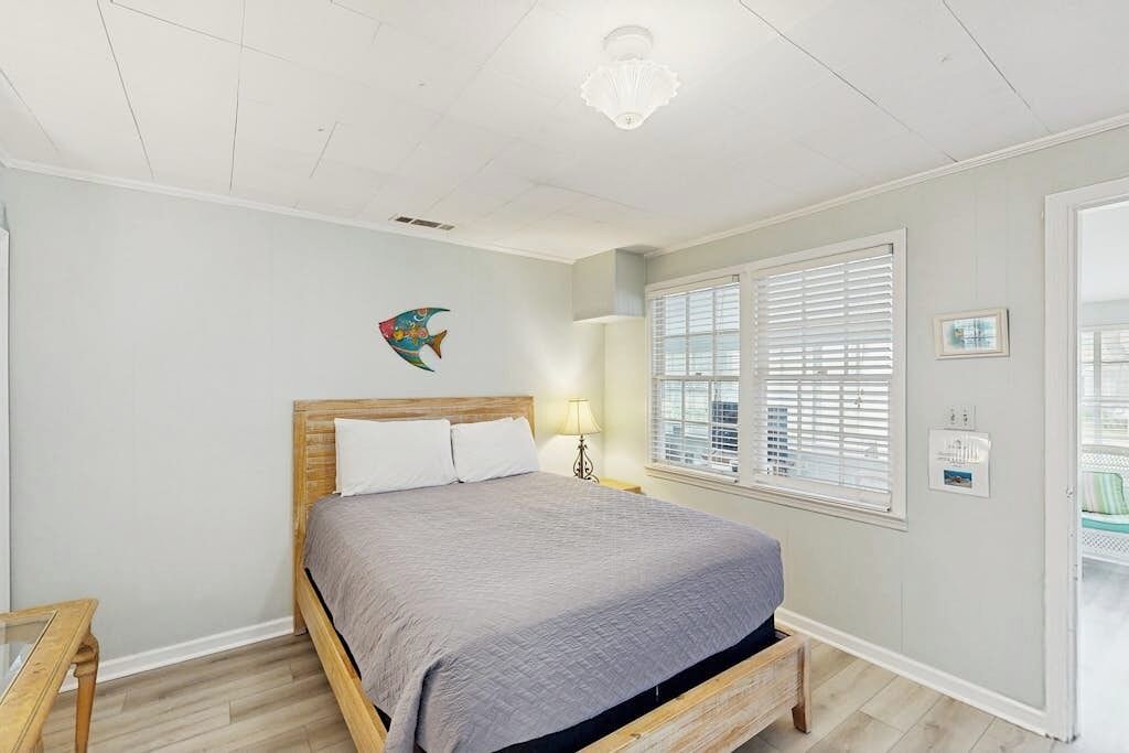 Une chambre à coucher comprenant un lit, une table de chevet, une lampe, une fenêtre avec des stores et un élément de décoration murale.