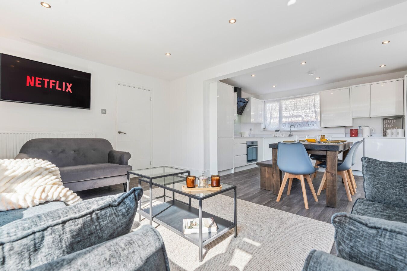 Una sala de estar moderna con un sofá gris, una mesa de centro de vidrio y un televisor de pantalla plana mostrando 'NETFLIX'.