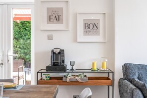 Un espacio habitable moderno con una cafetera, un vaso de agua y un cartel enmarcado que dice 'BON appétit' en la pared.