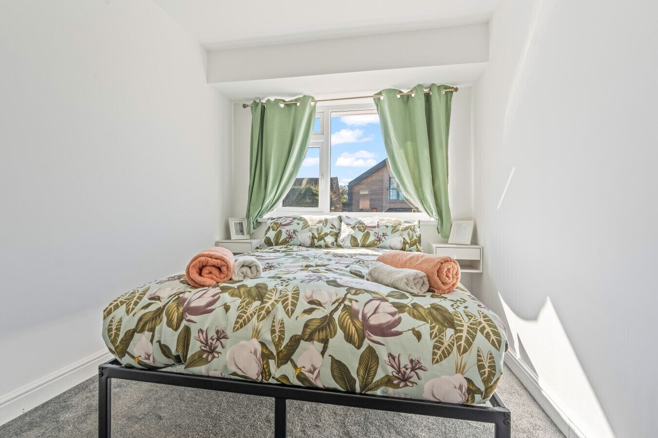 A bedroom with a bed, green curtains, a window, and a view of a building outside.