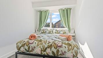 Un dormitorio con cama, cortinas verdes, una ventana y vistas a un edificio.