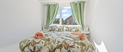 A bedroom with a bed, green curtains, a window, and a view of a building outside.