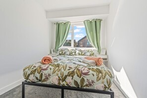 Een slaapkamer met een bed, groene gordijnen, een raam en uitzicht op een gebouw.