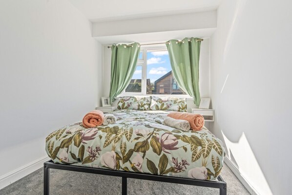 Une chambre à coucher avec un lit, des rideaux verts, une fenêtre et une vue sur un bâtiment à l’extérieur.