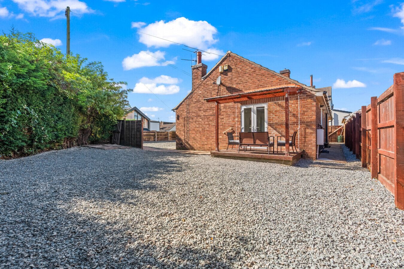 A gravel driveway leading to a brick house with a covered porch and a small garden area.