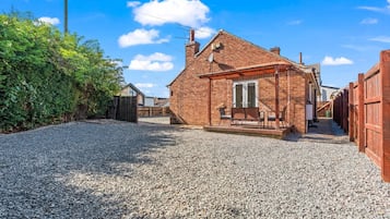 A gravel driveway leading to a brick house with a covered porch and a small garden area.
