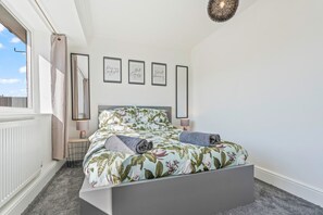 Ein Schlafzimmer mit einem Bett, einem Nachttisch, einer Lampe und einem Fenster mit Vorhängen.