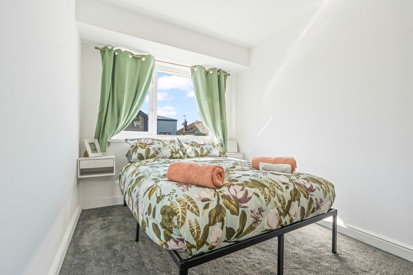Un dormitorio con cama, cortinas verdes, una mesita de noche y una ventana.