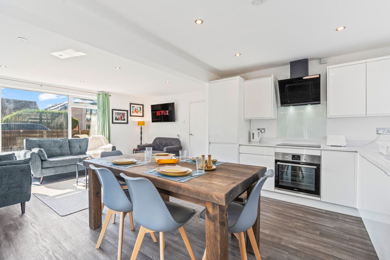 A modern kitchen with white cabinets, a built-in oven, and a flat-screen TV.