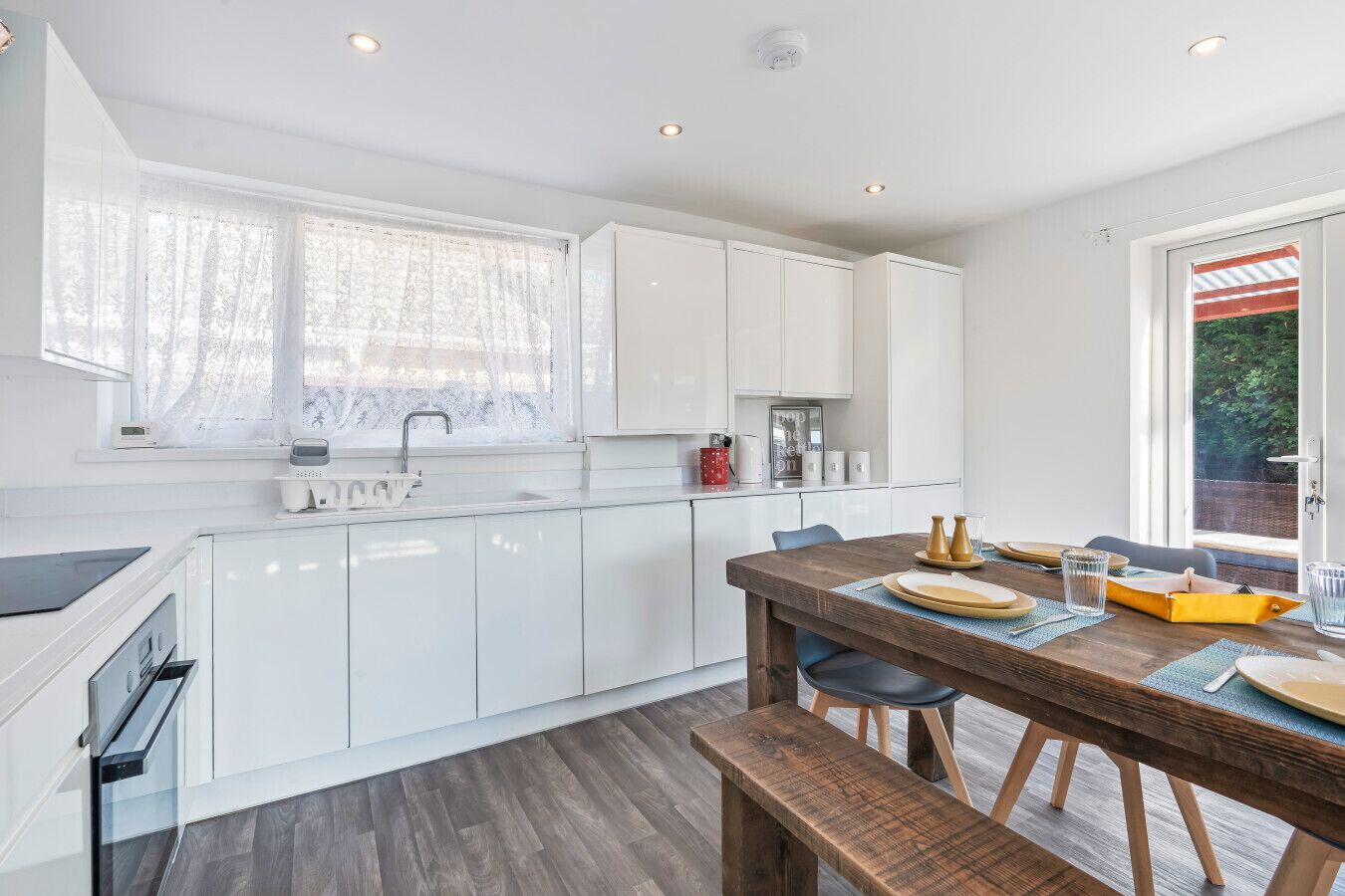 Una cocina moderna con armarios blancos, una mesa de comedor de madera y un banco.
