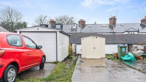 En röd bil parkerad på en uppfart, med ett garage och ett förråd i bakgrunden.