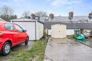 Ein rotes Auto steht auf einer Auffahrt, im Hintergrund sind eine Garage und ein Schuppen zu sehen.