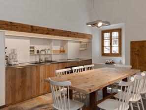A modern kitchen with a wooden island, white chairs, and a large dining table. - Chalet Ches'Ota by Interhome (La Punt-Chamues-ch)