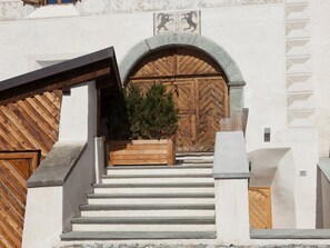 A staircase leading to a wooden door with a lion emblem, a small tree, and a stone plaque above the door. - Chalet Ches'Ota by Interhome (La Punt-Chamues-ch)