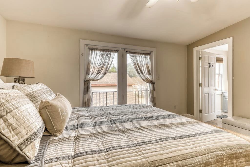 Une chambre à coucher avec un lit, des rideaux, une lampe et une vue sur l’extérieur.