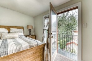 A bedroom with a wooden bed, a nightstand, a lamp, and a view of a balcony with greenery. - Modern Historic District duplex spacious and short walk to parks and restaurants (Savannah)