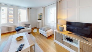 Una sala de estar moderna con una televisión de pantalla plana, un sofá, una mesita de centro y un pequeño taburete.