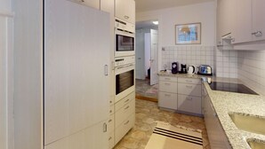 Una cocina con gabinetes blancos, microondas, horno y cafetera.