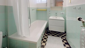 Baño con bañera, lavamanos y piso a cuadros.