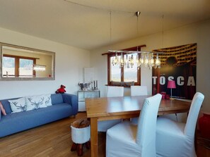 A modern living room with a blue sofa, a wooden dining table, and a chandelier. - Apartment Cuntainta Madulain by Interhome (Madulain)