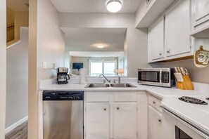 A modern kitchen with white cabinetry, a built-in microwave, and a dishwasher. - Oceanfront gem with spacious deck, direct beach access, & high-speed WiFi (Tybee Island)