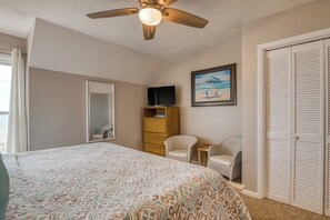 Une chambre à coucher comprenant un lit, un ventilateur de plafond, une télévision, une commode, deux chaises, un tableau et un placard.
