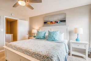A bedroom with a bed, nightstands, a ceiling fan, and a wall-mounted light fixture. - Oceanfront gem with spacious deck, direct beach access, & high-speed WiFi (Tybee Island)