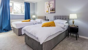 Una camera d'albergo con due letti, una finestra con tende, un comodino con una lampada e un quadro appeso al muro.