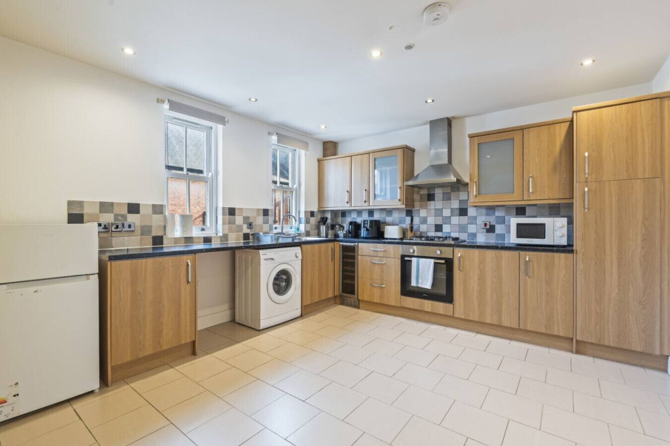 A modern kitchen with wooden cabinets, a built-in washing machine, and a microwave.