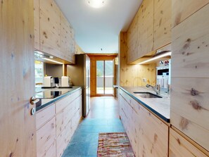 A modern kitchen with wooden cabinetry, a central island, and a view to the outdoors. - Apartment Sur Puoz 1A by Interhome (Samedan)
