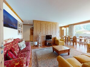 A cozy living room with a sofa, a coffee table, a TV, and a dining area with chairs and a table. - Apartment Sur Puoz 1A by Interhome (Samedan)