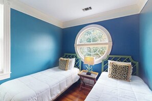 Een slaapkamer met twee eenpersoonsbedden, een rond raam en een klein tafeltje met een lamp.