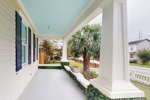A covered porch with white columns, a palm tree, and a white picket fence. - Designer home in Historic District with upscale kitchen (Savannah)