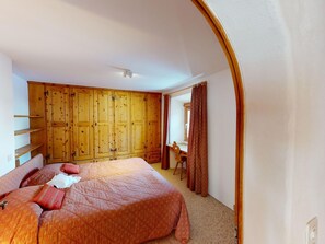 A bedroom with a large bed, wooden wardrobe, and a desk with a chair. - Apartment Paterna 9 by Interhome (La Punt-Chamues-ch)