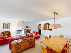 A living room with a fireplace, red sofa, wooden coffee table, and a dining table with chairs. - Apartment Paterna 9 by Interhome (La Punt-Chamues-ch)