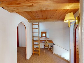 A narrow hallway with a wooden ceiling, a wooden ladder, a desk with a chair, and a wall-mounted lamp. - Apartment Paterna 9 by Interhome (La Punt-Chamues-ch)