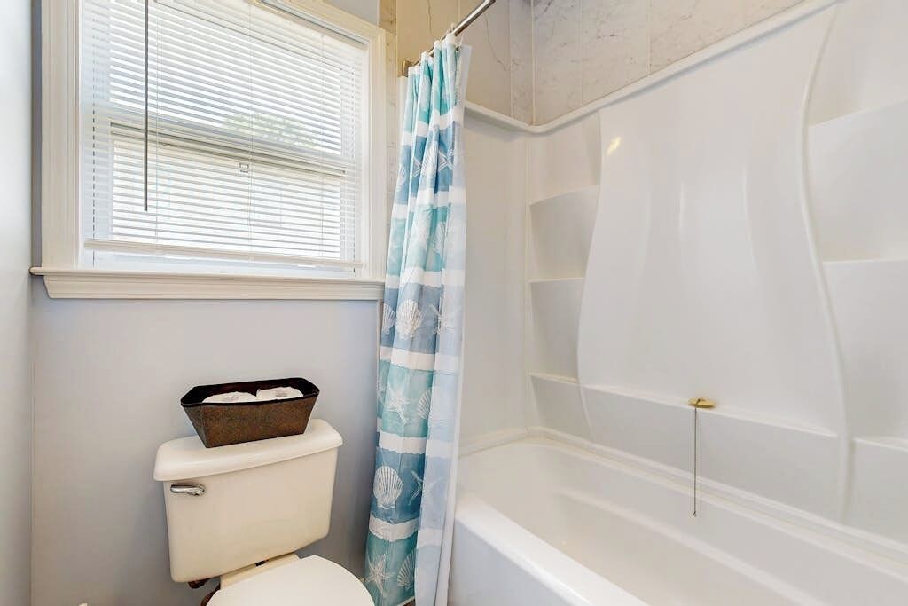 A bathroom with a toilet, a bathtub, and a window with blinds.