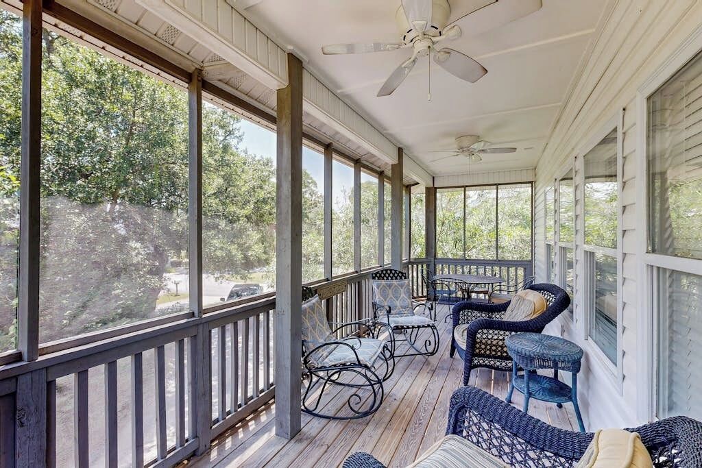 A covered porch with a ceiling fan, wicker furniture, and large windows offering a view of the outdoors.