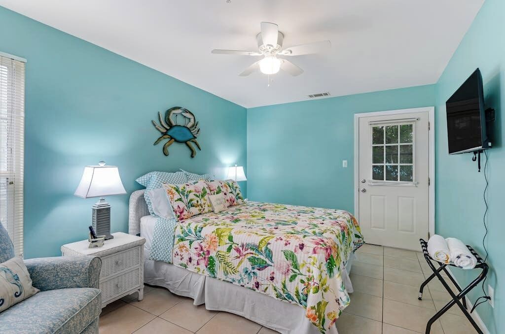 A bedroom with a bed, nightstand, chair, and a wall-mounted TV.