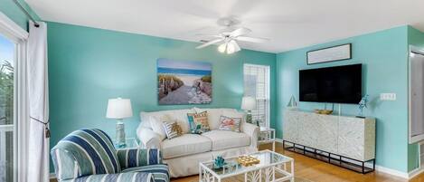 A living room with a teal wall, a white ceiling fan, a large TV, and a sofa with striped cushions.