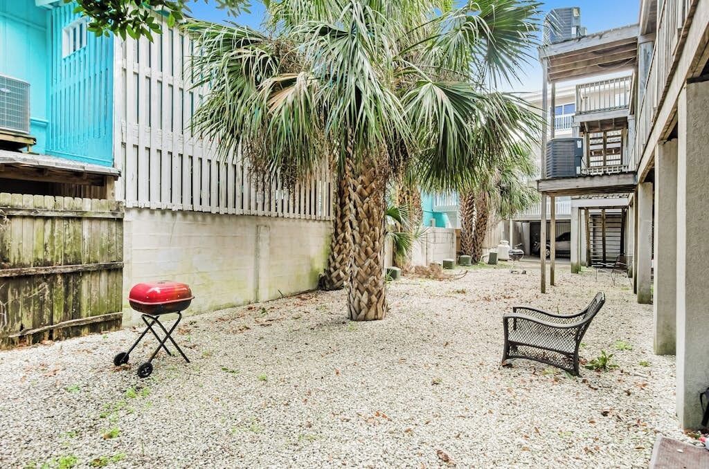 A courtyard with a palm tree, a barbecue grill, and a bench.