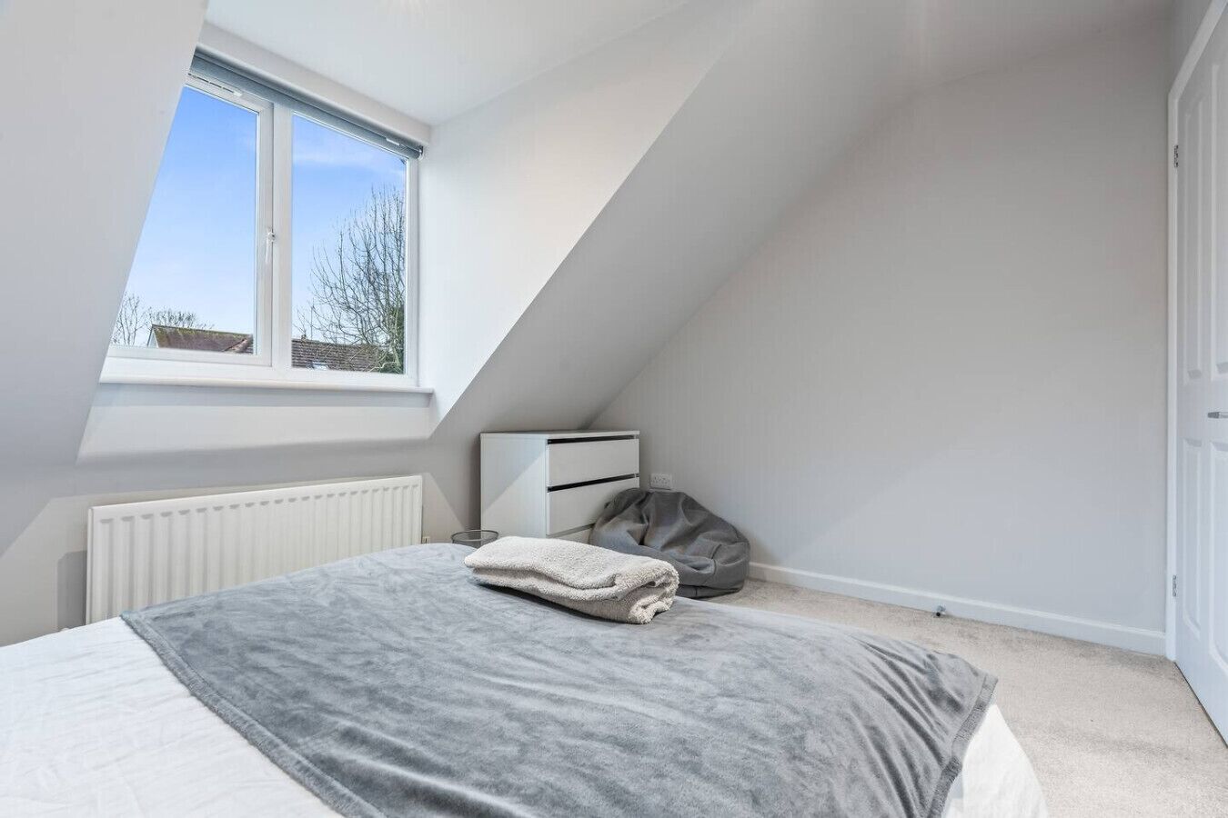 Une chambre à coucher avec un lit, un radiateur, une fenêtre et une armoire blanche.