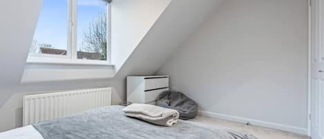 A bedroom with a bed, a radiator, a window, and a white wardrobe.