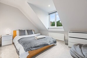 Een moderne slaapkamer met een schuine plafond, een groot bed, nachtkastjes, een dressoir en een raam met uitzicht.