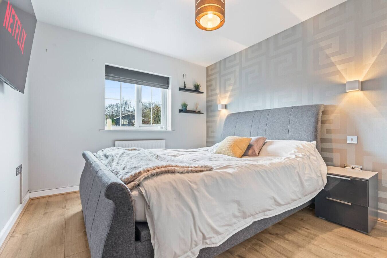 A modern bedroom with a large bed, bedside tables, a window, and a wall-mounted light fixture.