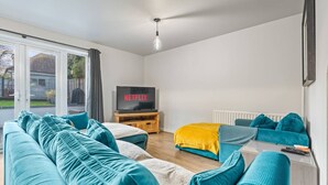 Ett modernt vardagsrum med en soffgrupp, en tv-apparat på ett träbord och utsikt genom en glasdörr.