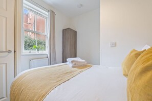A hotel room with a bed, a window with curtains, a radiator, and a wardrobe. - Central Derby Stay | Comfort for 4 | Wi-Fi (Derby)