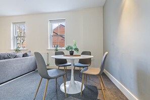 Una habitación moderna con una mesa redonda, cuatro sillas, un sofá gris y dos ventanas.