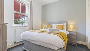 Ein Schlafzimmer mit einem großen Bett, einem Nachttisch mit Lampe, einem Fenster mit Vorhängen und einer Heizung.