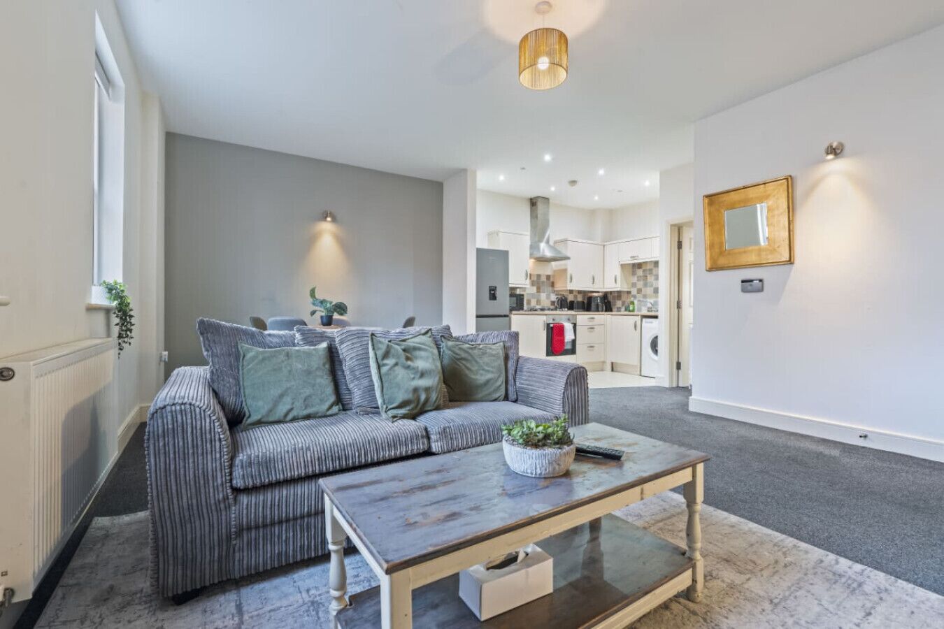A modern living room with a sofa, a coffee table, and a kitchen in the background.
